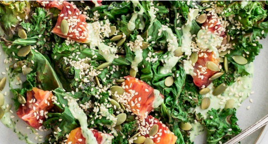 Close-up of lightly charred garden-fresh kale leaves drizzled with a pale green tahini and cilantro dressing on a ceramic plate.