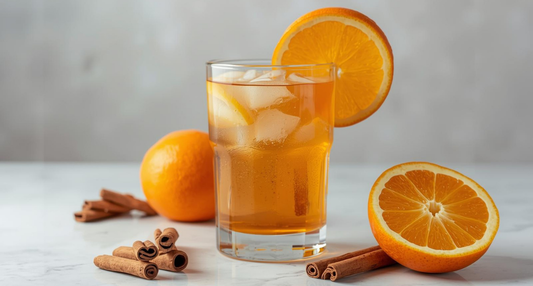 A refreshing glass of Fresh Cinnamon Orange Water with orange wedges, a cinnamon stick, and a vibrant sprig of garden-grown rosemary.