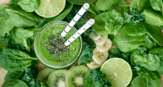 Close-up of a vibrant green smoothie in a glass, surrounded by fresh-picked kale and spinach leaves on a wooden surface.