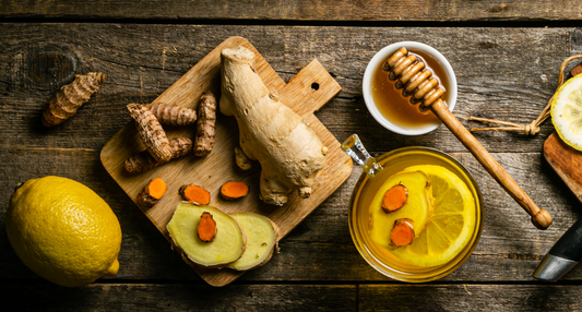 High-angle shot of a steaming glass mug of golden turmeric and ginger tea with floating lemon slices and a honey dipper.